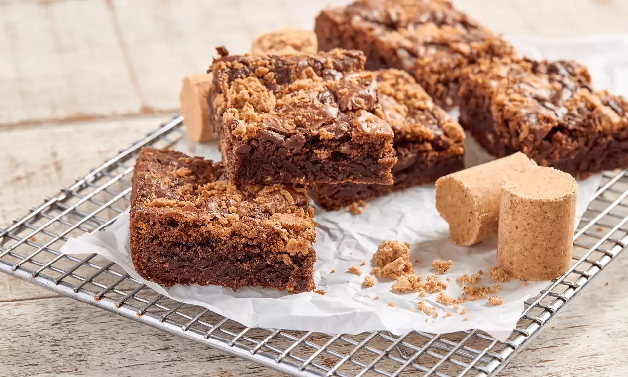 Brownies de chocolate escuro com textura macia e crocante, cobertos com farofa de paçoca, dispostos sobre papel branco em uma grade metálica