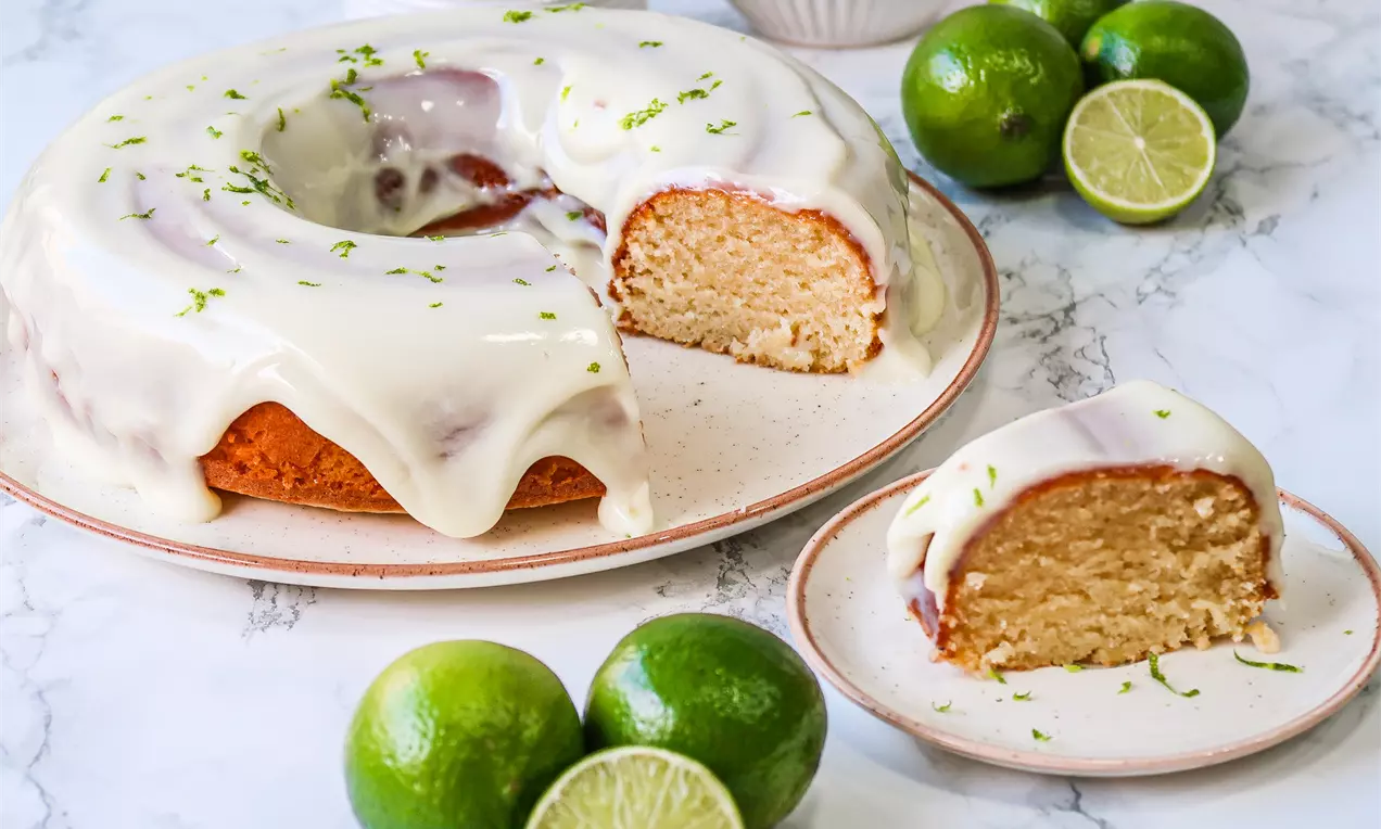 Bolo de limão cremoso com cobertura de glacê e raspas amarelas, decorado com fatias finas de limão e folhas verdes sobre prato branco