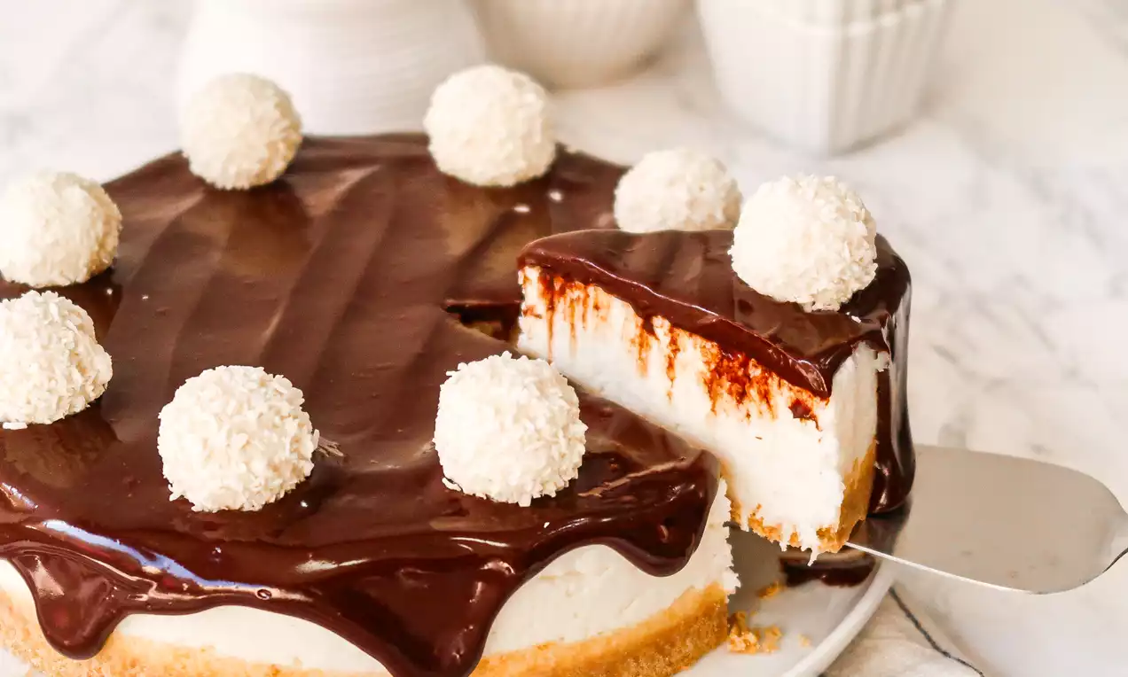 Torta gelada com base dourada de biscoito, recheio branco cremoso, cobertura lisa de ganache escuro e decorada com bolas de coco