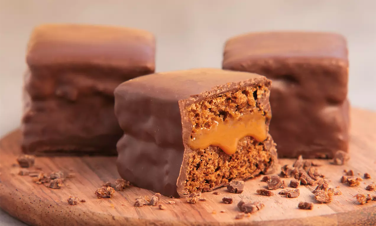Pão de mel glaceado com chocolate, fatias mostrando miolo dourado, dispostos em prato branco com chocolate ralado e fio de mel