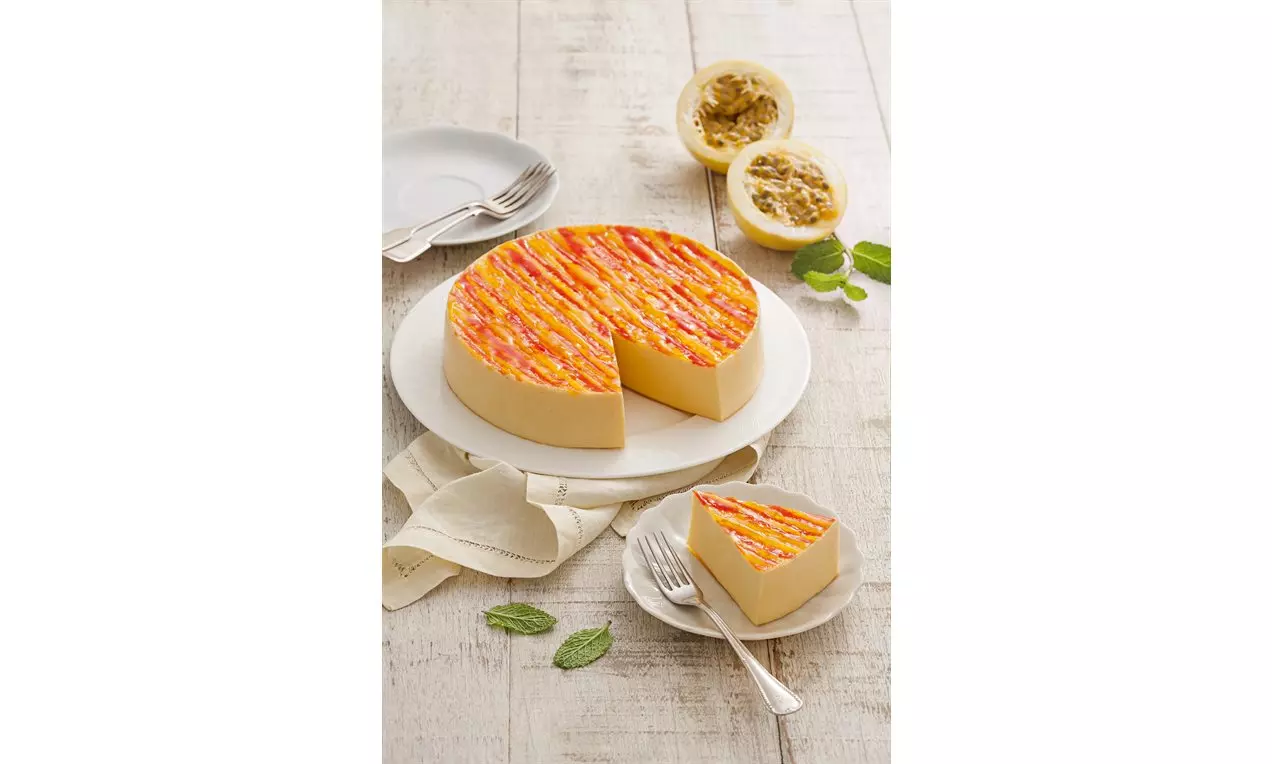 Torta redonda de maracujá com superfície amarela e listras alaranjadas brilhosas, acompanhada de fatia em prato branco com talheres