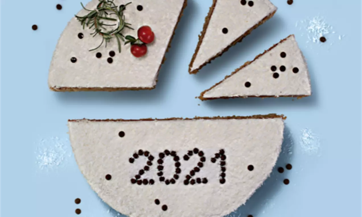 Bolo redondo coberto com glacê branco, decorado com romãs e alecrim, dividido em fatias e salpicado com pequenas esferas de chocolate
