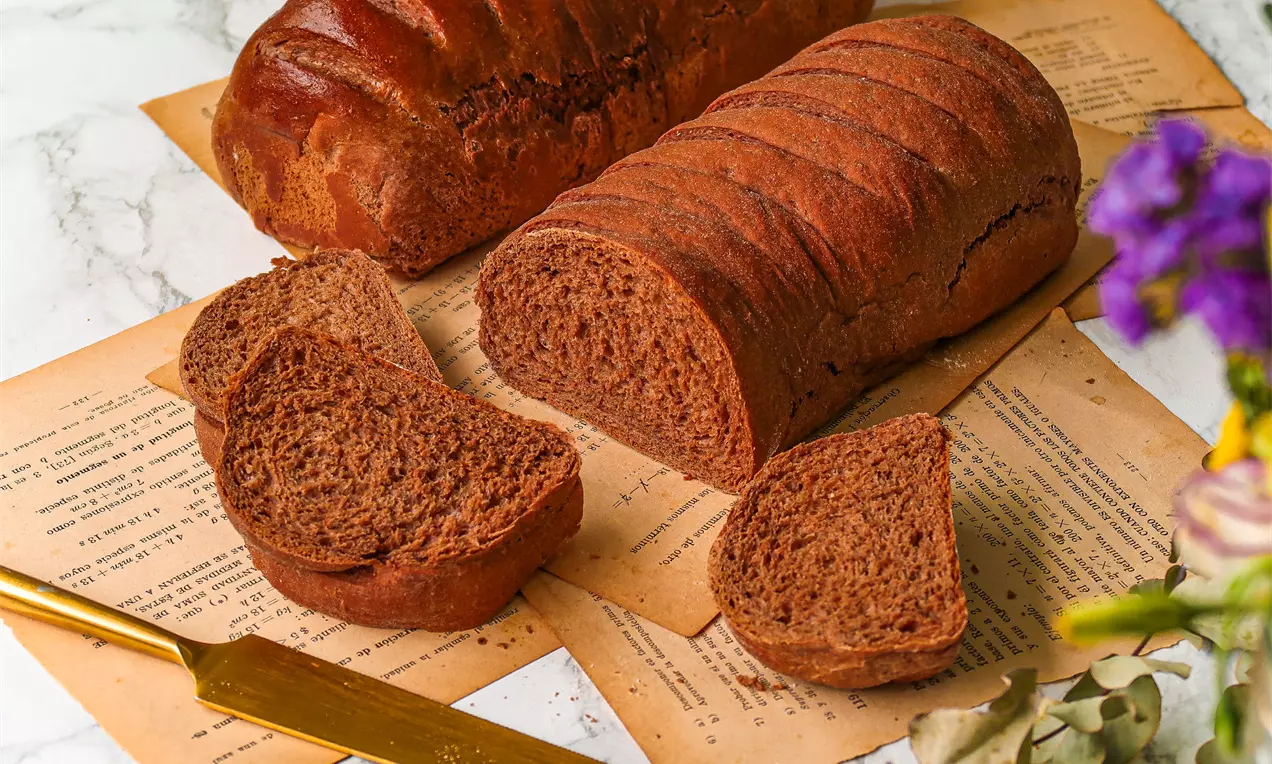 Pão australiano dourado com crosta brilhante, fatias mostrando miolo macio e amarelado, sobre tábua com manteiga e alecrim