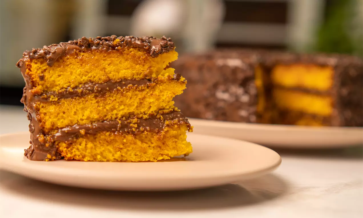 Fatias de bolo dourado com textura macia intercaladas por camadas de brigadeiro escuro cremoso em prato bege sobre mesa clara