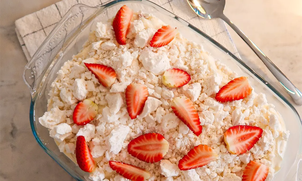 Camada de chantilly com textura cremosa coberta por merengues quebrados e morangos vermelhos fatiados dispostos em travessa de vidro