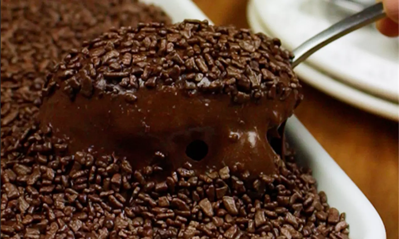 Brownie denso com ganache de creme de avelã brilhante, coberto com granulado de chocolate em uma travessa branca