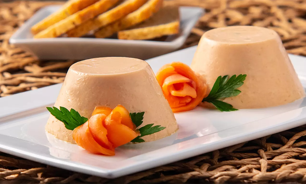 Flans individuais de salmão defumado com textura lisa em tom salmão claro, decorados com rosas de salmão, folhas de salsinha e torradas ao fundo
