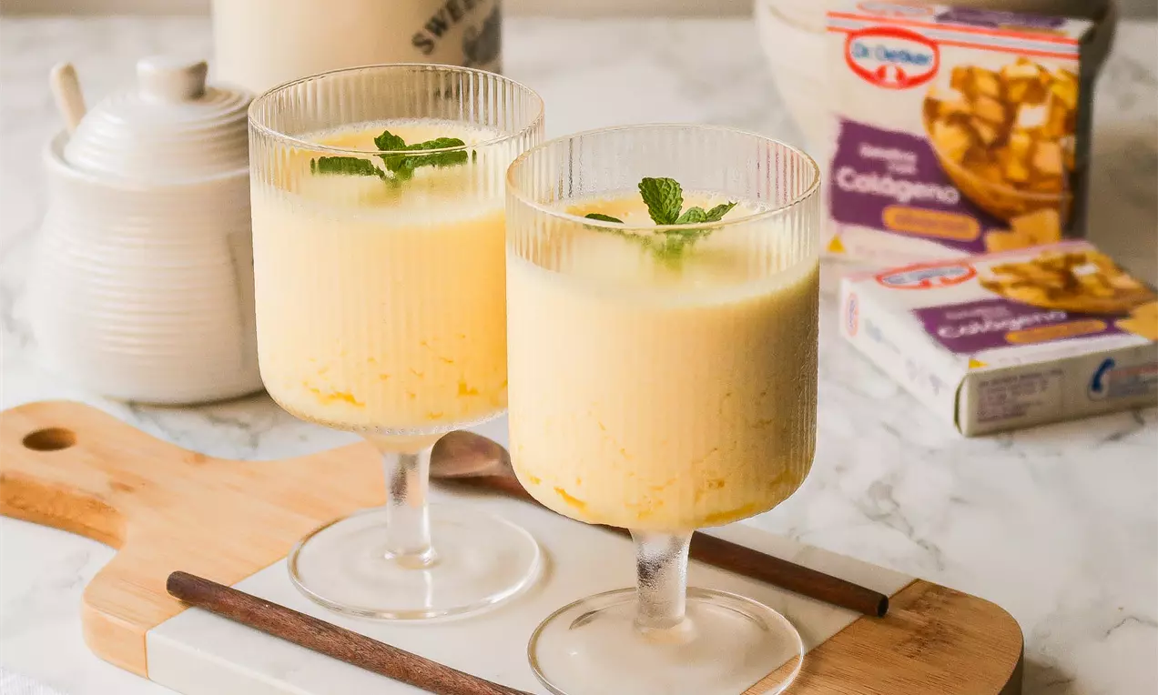 Gelatina cremosa de abacaxi com tom amarelo claro, textura leve e uniforme, decorada com folhas de hortelã em taças de vidro sobre tábua de madeira