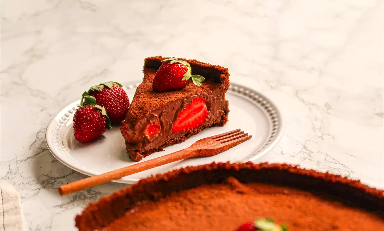 Fatia de torta de massa marrom com recheio cremoso de chocolate e morangos inteiros, decorada com morangos frescos em um prato branco