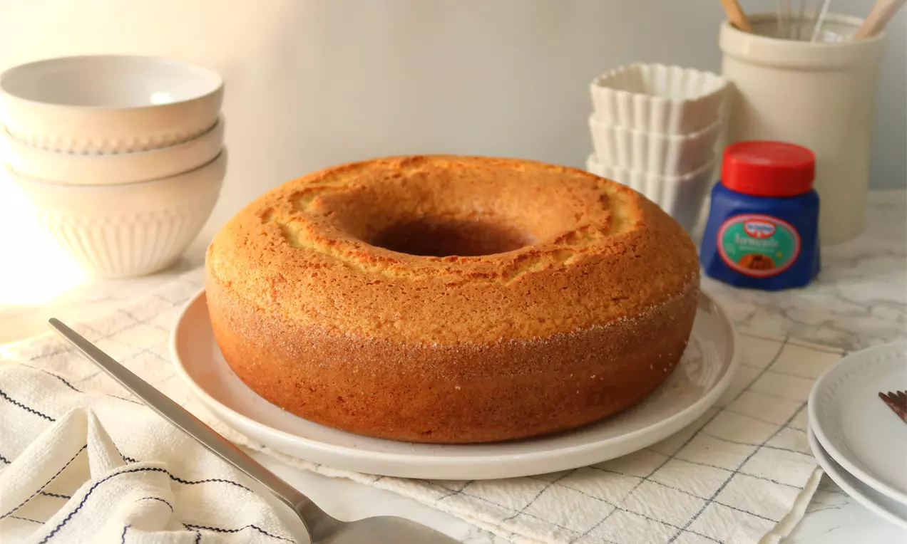 Bolo de fubá dourado com textura macia e bordas ligeiramente crocantes, em formato redondo com furo central sobre prato branco