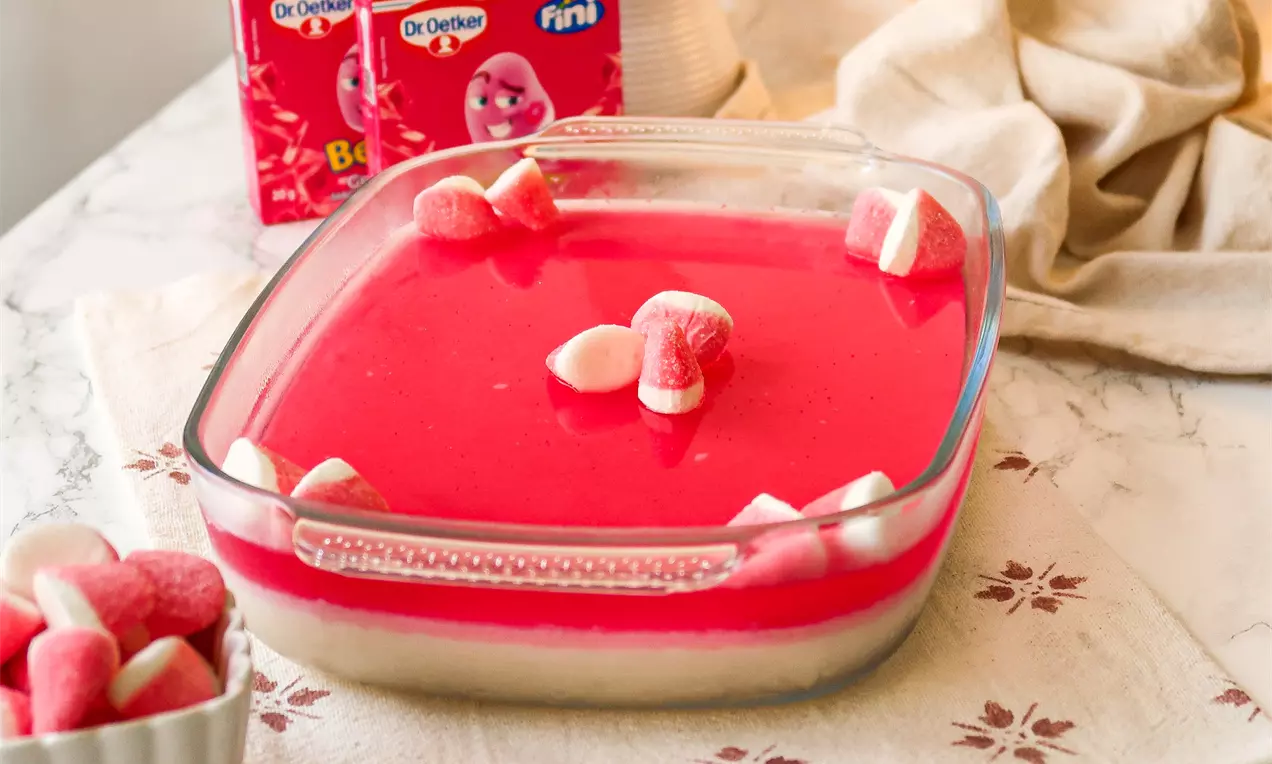 Camada cremosa branca coberta por gelatina rosa brilhante com marshmallows rosados e brancos flutuando em uma travessa de vidro