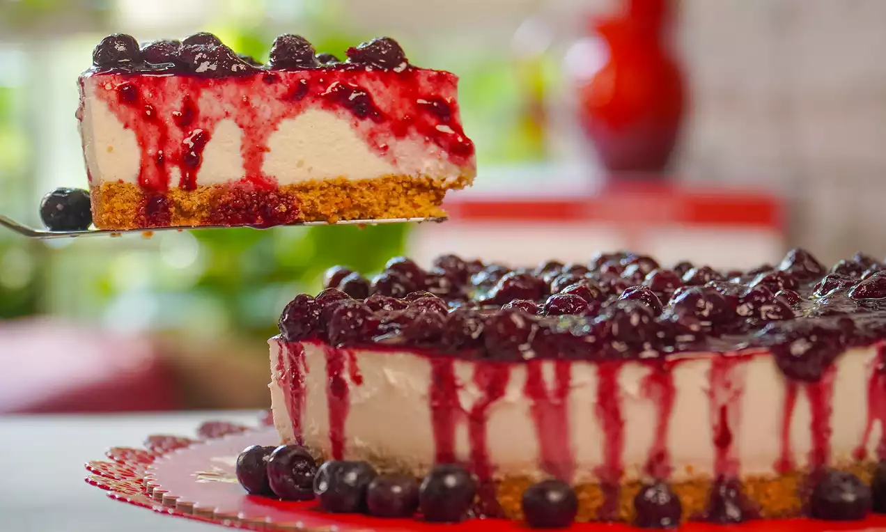 Cheesecake de frutas vermelhas com base dourada de biscoito, recheio claro e cobertura brilhante de calda e frutas inteiras em prato decorativo