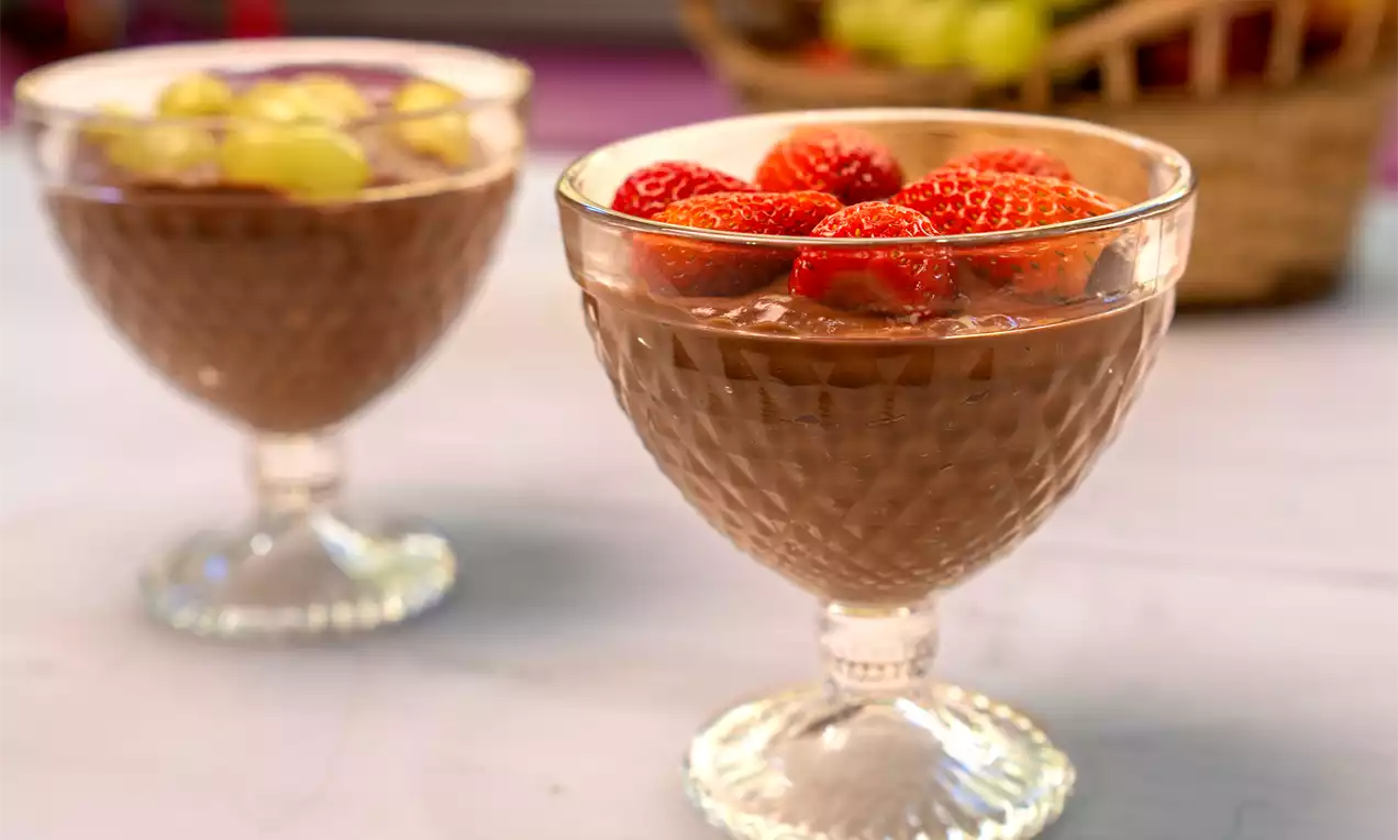 Creme de chocolate marrom cremoso em taças de vidro texturizado, decorado com morangos vermelhos frescos sobre superfície clara