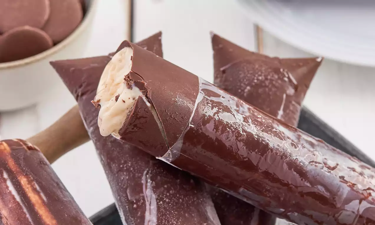 Geladinho gourmet com casca crocante dourada e recheio cremoso branco, servido em palitos, decorado com raspas de chocolate
