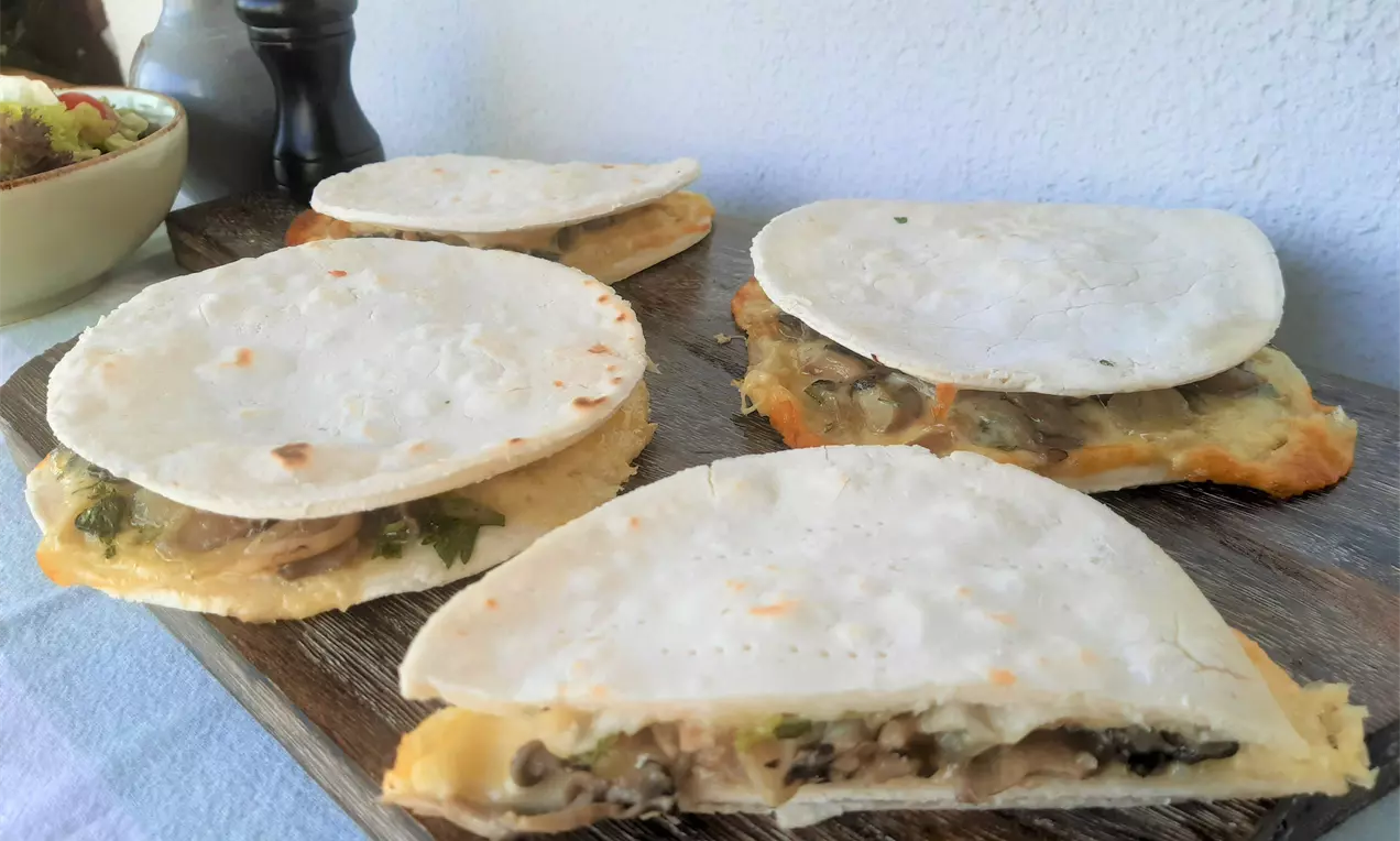 Quesadillas de massa fina e clara ligeiramente tostada, recheadas com vegetais picados e dispostas sobre tábua de madeira