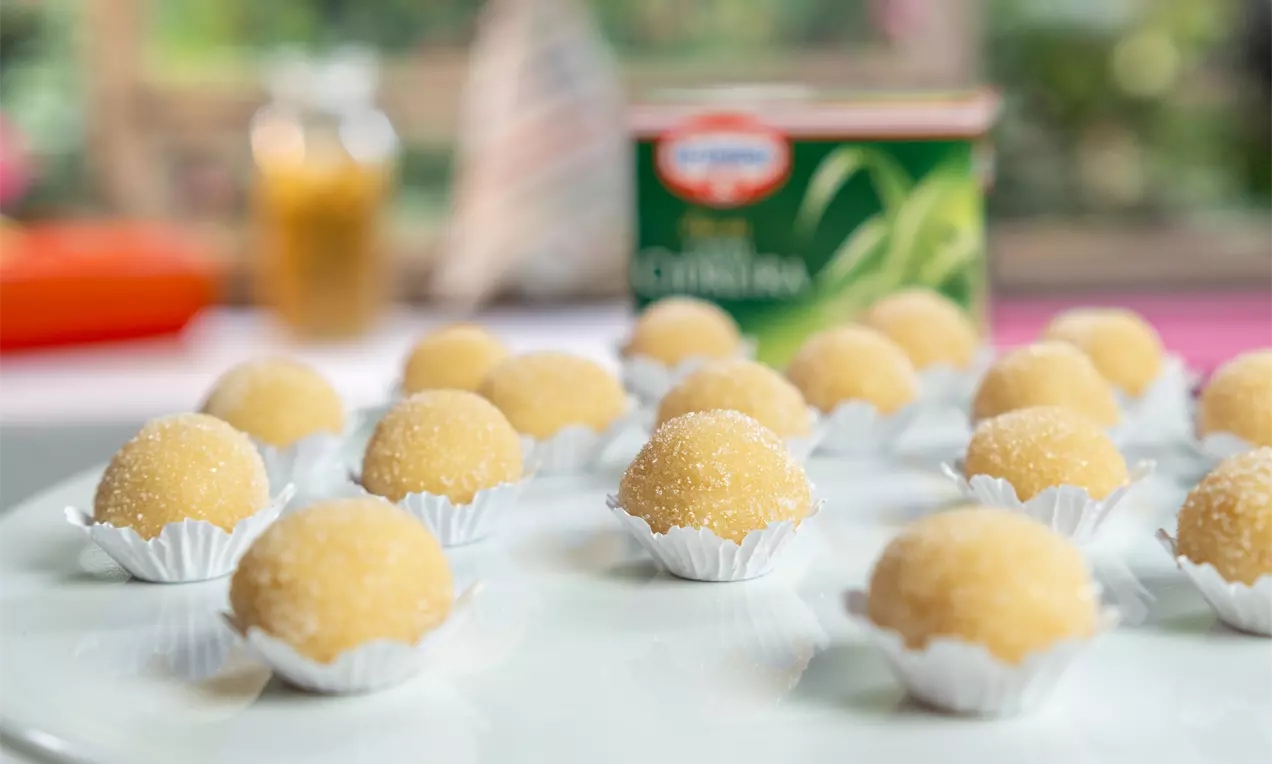 Brigadeiros arredondados de chá verde em tom amarelo-claro, revestidos de açúcar cristal, dispostos em forminhas sobre prato branco
