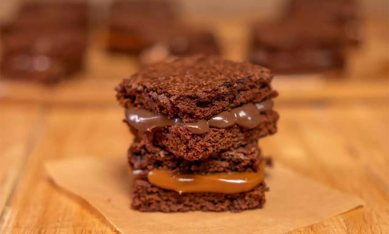 Sanduíche de camadas de brownies macios e quebradiços, recheado com creme de chocolate escuro e doce de leite sobre papel manteiga